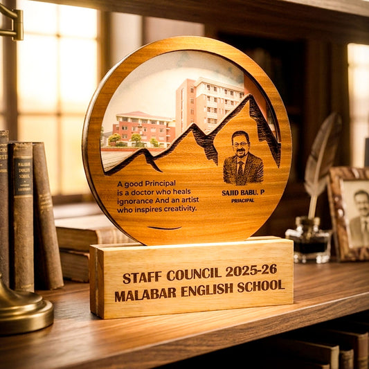 A personalized wooden staff council award plaque on a matching wooden base, displayed on a bookshelf. The circular plaque features a laser-engraved portrait of Principal Said Barli, a school building, mountain silhouettes, and a quote.