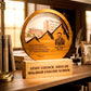 A personalized wooden staff council award plaque on a matching wooden base, displayed on a bookshelf. The circular plaque features a laser-engraved portrait of Principal Said Barli, a school building, mountain silhouettes, and a quote.