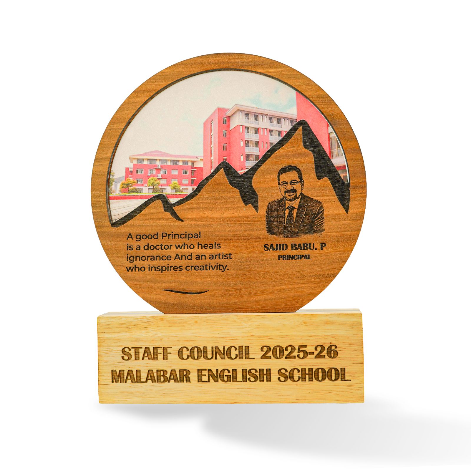 A custom wooden school staff council award plaque on a light wood base. The round wooden top features an engraved portrait of Principal Said Babu, a mountain silhouette, a school building illustration, and a quote.
